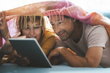Älterer Mann und Frau mit gemeinsamem Tablet-PC unter einer Decke liegend zu Hause - JOSEF10406