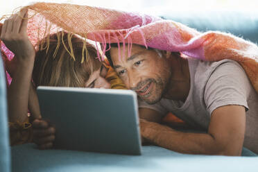 Älterer Mann mit Frau, die einen Tablet-PC benutzt, unter einer Decke liegend - JOSEF10407