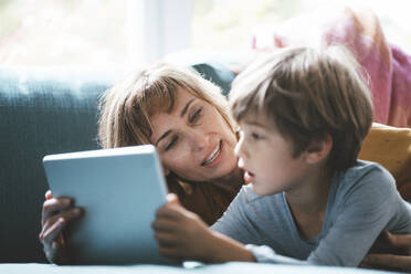 Mature woman with boy with tablet PC lying on sofa at home - JOSEF10417