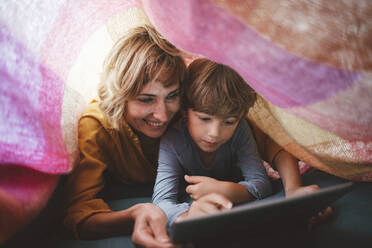 Cute boy with mother using tablet PC under blanket - JOSEF10418