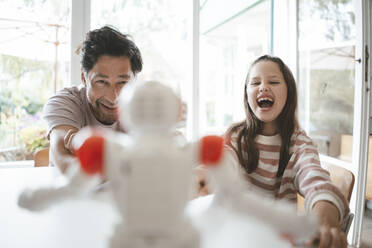 Happy father and daughter playing with toy robot at home - JOSEF10423