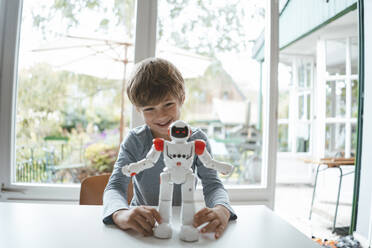 Happy boy with toy robot sitting at table - JOSEF10430