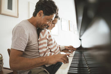 Happy father teaching piano to daughter at home - JOSEF10432