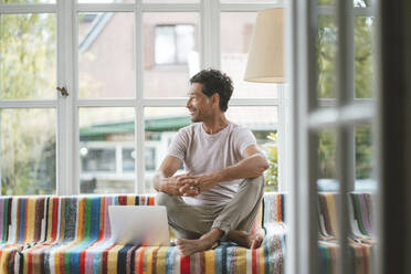 Älterer Mann mit Laptop sitzt zu Hause auf dem Sofa - JOSEF10434