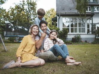 Happy family sitting on grass in back yard - JOSEF10443