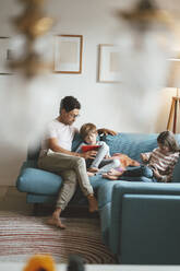 Vater sitzt mit Sohn und Tochter auf dem Sofa und benutzt einen Tablet-PC - JOSEF10451