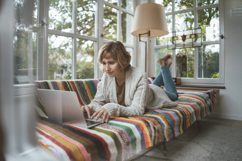 Lächelnde Frau mit Laptop auf dem Sofa zu Hause liegend - JOSEF10455