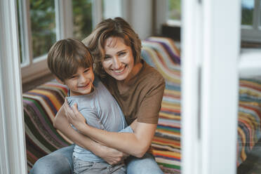 Happy mature woman embracing son seen through window - JOSEF10475