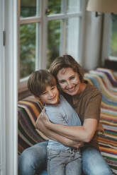 Glückliche Frau mit Sohn sitzt zu Hause auf dem Sofa - JOSEF10476