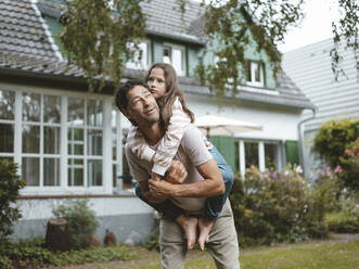 Father giving piggyback ride to daughter in front of house - JOSEF10485