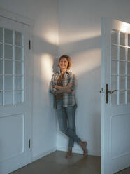 Happy woman leaning on wall by door - JOSEF10506