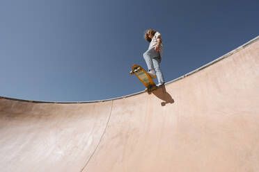 Junger Mann mit Skateboard auf einer Sportrampe an einem sonnigen Tag - MMPF00079