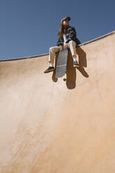 Frau mit Skateboard auf einer Sportrampe an einem sonnigen Tag - MMPF00083
