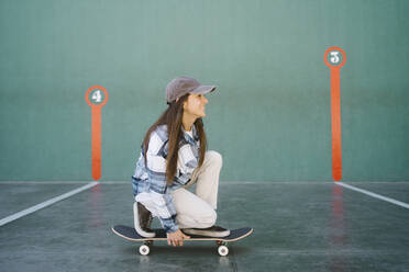 Smiling woman on skateboard in front of green wall - MMPF00091