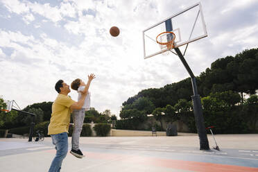 Vater mit Sohn beim Basketballwerfen auf dem Sportplatz - MMPF00109