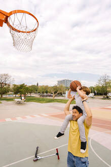 Boy with basketball sitting on father's shoulders at sports court - MMPF00112