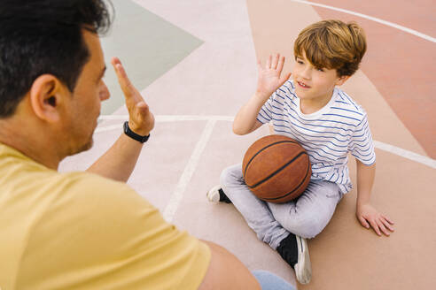 Boy with basketball giving high five to father at sports court - MMPF00113