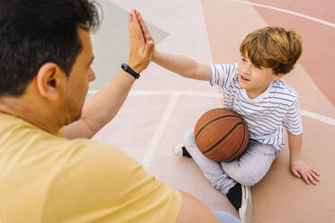 Junge mit Basketball, der einem Mann auf dem Sportplatz ein High Five gibt - MMPF00114