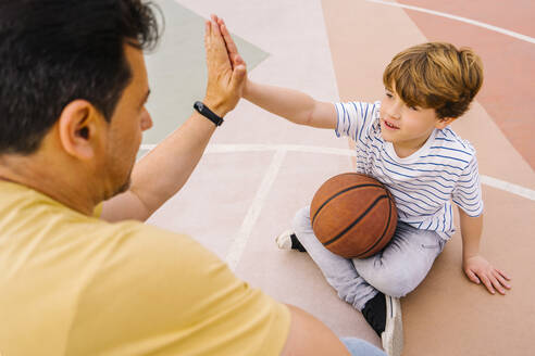 Boy with basketball giving high five to man at sports court - MMPF00114