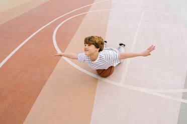 Verspielter Junge mit ausgestreckten Armen auf einem Basketball balancierend - MMPF00116