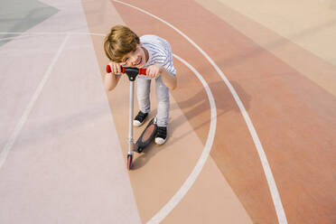 Smiling boy with push scooter at sports court - MMPF00117