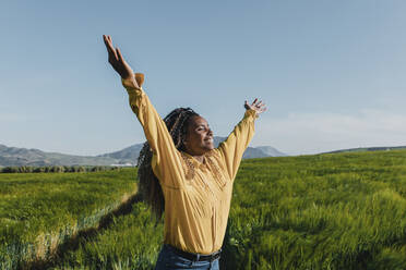 Happy young woman with arms raised in meadow - DMGF00745