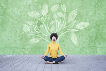 Young woman meditating under tree painted on wall - UUF26463