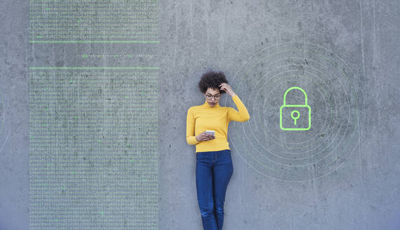 Confused woman looking at smartphone with data lock painted on wall - UUF26471