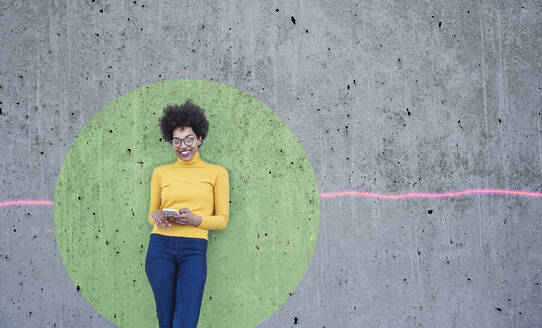 Frau mit Smartphone, die sich an eine Wand mit grünem Kreis lehnt - UUF26472