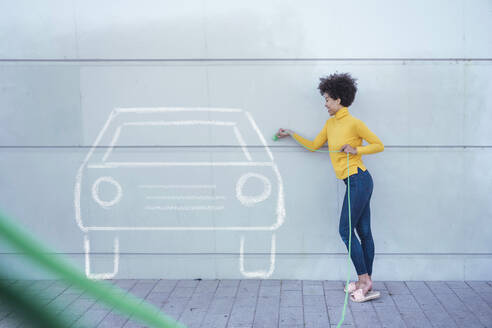 Junge Frau, die ein lackiertes Auto mit grünem Stecker zurücksetzt - UUF26474