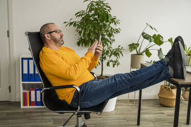 Businessman using smart phone with feet on desk in office - OSF00012