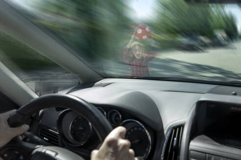 Scared boy with ball seen through windshield of car trying to prevent accident - RNF01388