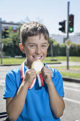 Lächelnder Junge zeigt goldene Medaille an einem sonnigen Tag - RNF01392
