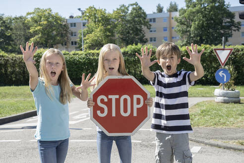 Girl holding stop sign board standing by friends on sunny day - RNF01396