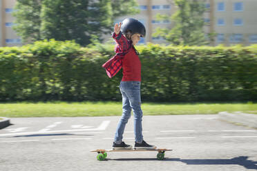 Junge mit ausgestreckten Armen auf dem Skateboard im Straßenverkehr - RNF01397
