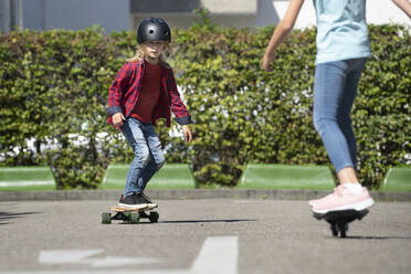 Junge mit Helm fährt mit einem Freund Skateboard auf einem Verkehrskurs - RNF01399