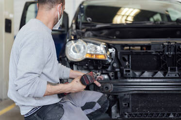 Automechaniker repariert Auto mit elektrischem Schraubenzieher in der Werkstatt - PGF01089