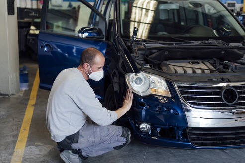 Auto mechanic analyzing car bumper in workshop - PGF01092