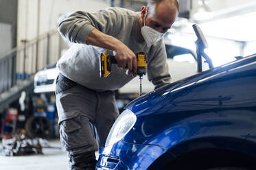 Automechaniker bei der Arbeit mit einem elektrischen Schraubenzieher in einer Werkstatt - PGF01094