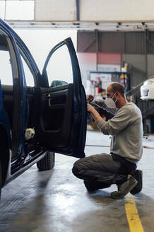 Auto mechanic working on car door in repair shop - PGF01097