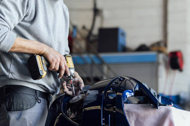 Hände eines Mechanikers bei der Reparatur eines Fahrzeugteils mit einem elektrischen Schraubenzieher in einer Werkstatt - PGF01110