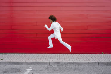 Fröhliche junge Frau, die über den Bürgersteig an der roten Wand springt - GIOF15502