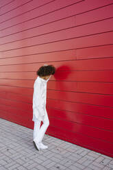 Afro woman standing on sidewalk by red wall - GIOF15509