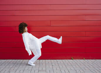 Young woman dancing on footpath by red wall - GIOF15511