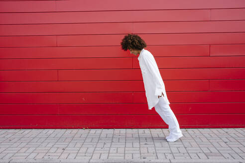 Young woman leaning forward by red wall - GIOF15515