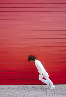 Junge Frau lehnt sich auf dem Fußweg an einer roten Mauer vor - GIOF15516