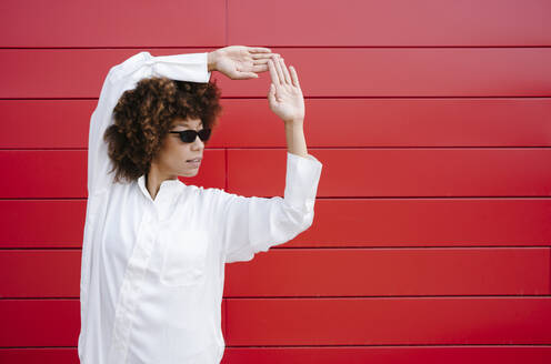 Afro-Frau mit Sonnenbrille macht Handzeichen vor einer roten Wand - GIOF15541