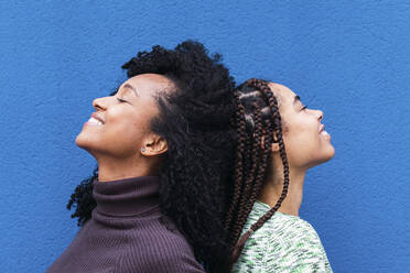 Glückliche multirassische Freunde stehen mit geschlossenen Augen vor einer blauen Wand - PNAF03931