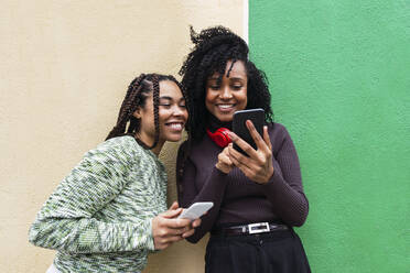 Happy multiracial friends with mobile phones standing in front of wall - PNAF03954