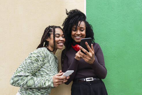 Fröhliche multirassische Freunde mit Handys vor einer Wand stehend - PNAF03954